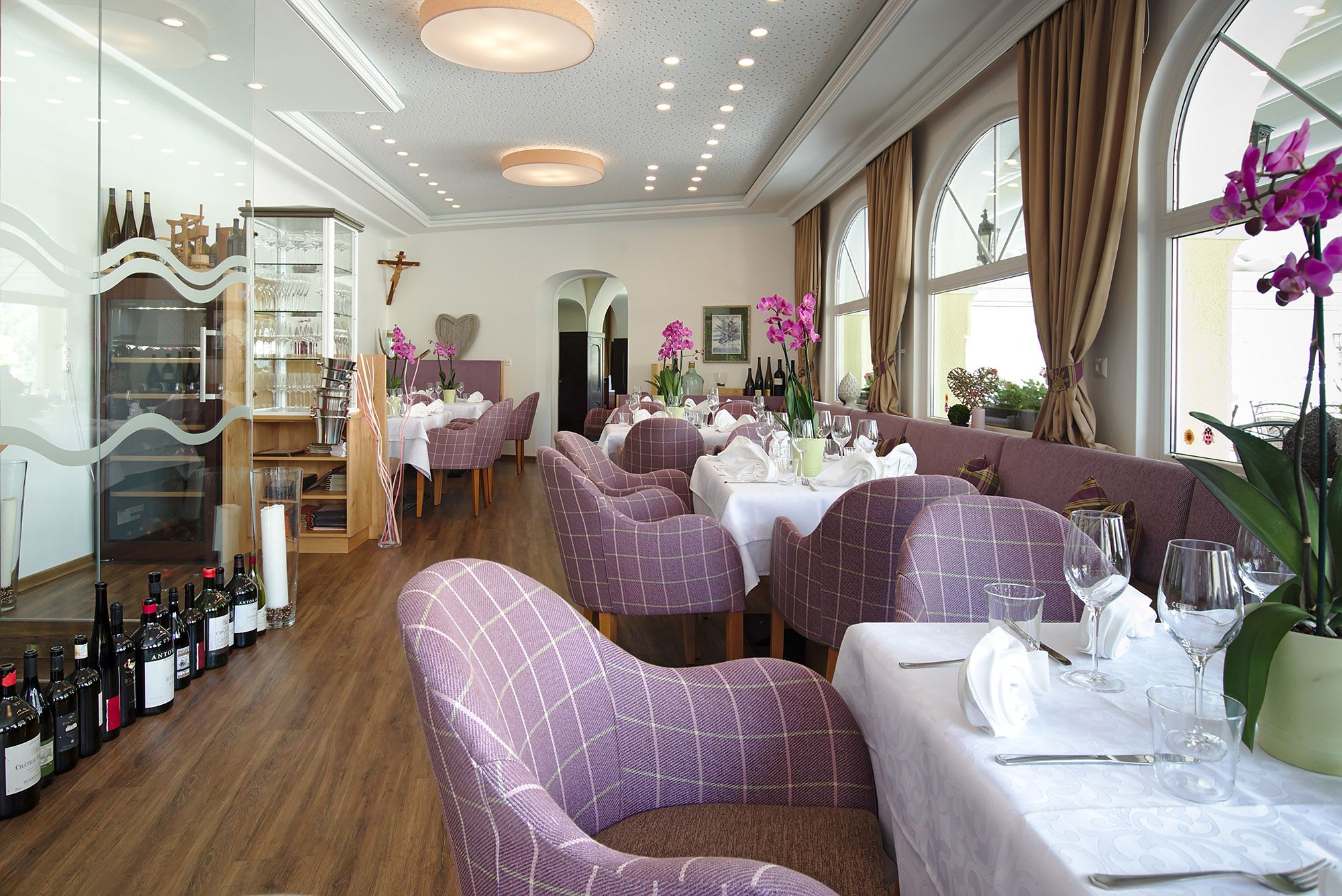 Elegantes Restaurant mit lila karierten Stühlen, weißen Tischdecken und Orchideen.
