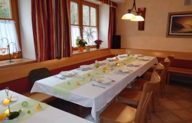 Ein festlich gedeckter Tisch in einem Gasthaus mit wei&szlig;en Tischdecken, Kerzen und Blumen. Holzm&ouml;bel und Fenster mit Vorh&auml;ngen im Hintergrund.