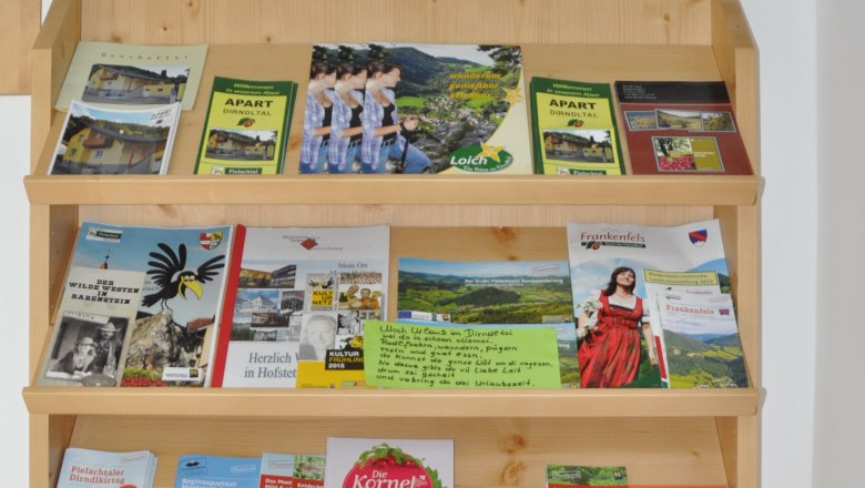 Ein Regal mit Broschüren und einem Schild mit 'Herzlich Willkommen Familie Krückel'.