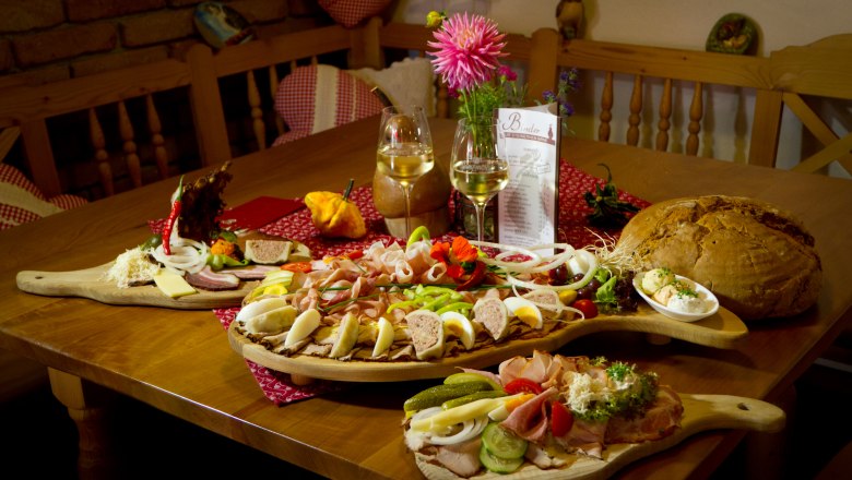 Ein Tisch mit einer Heurigenjause: Aufschnitt, Käse, Brot und Wein.