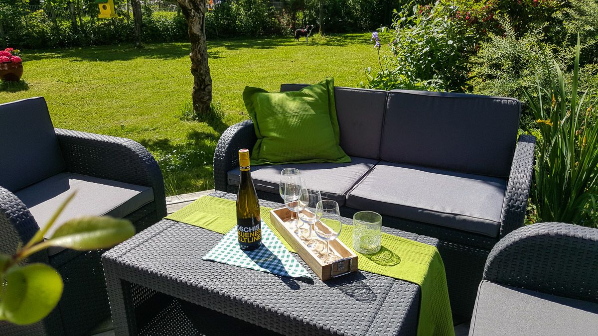 Gartenmöbel mit Weinflasche und Gläsern auf einem Tisch im Freien.