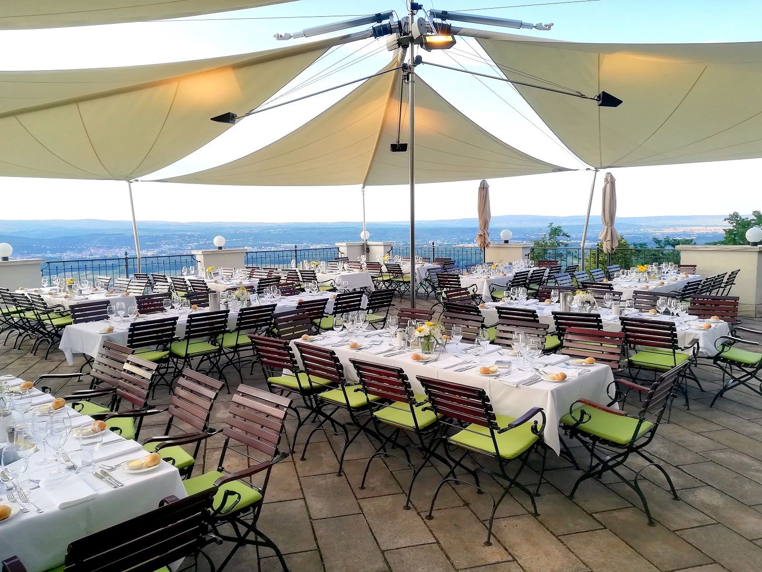 Gedeckte Tische auf einer Terrasse mit Blick auf die Landschaft, unter großen Sonnensegeln.