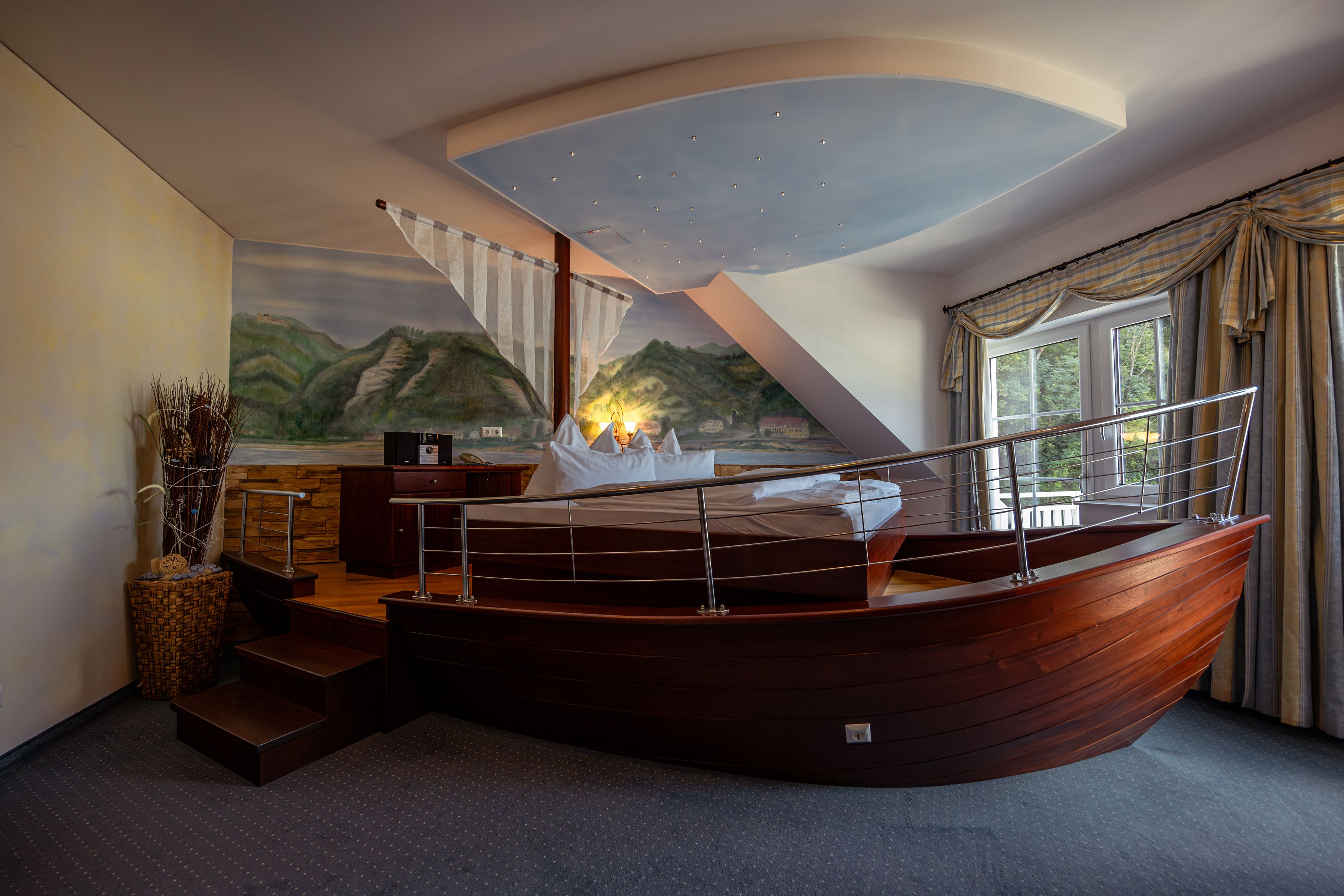 Hotelzimmer mit Bett in Form eines Bootes, Wandgemälde von Landschaft, Fenster mit Vorhängen.