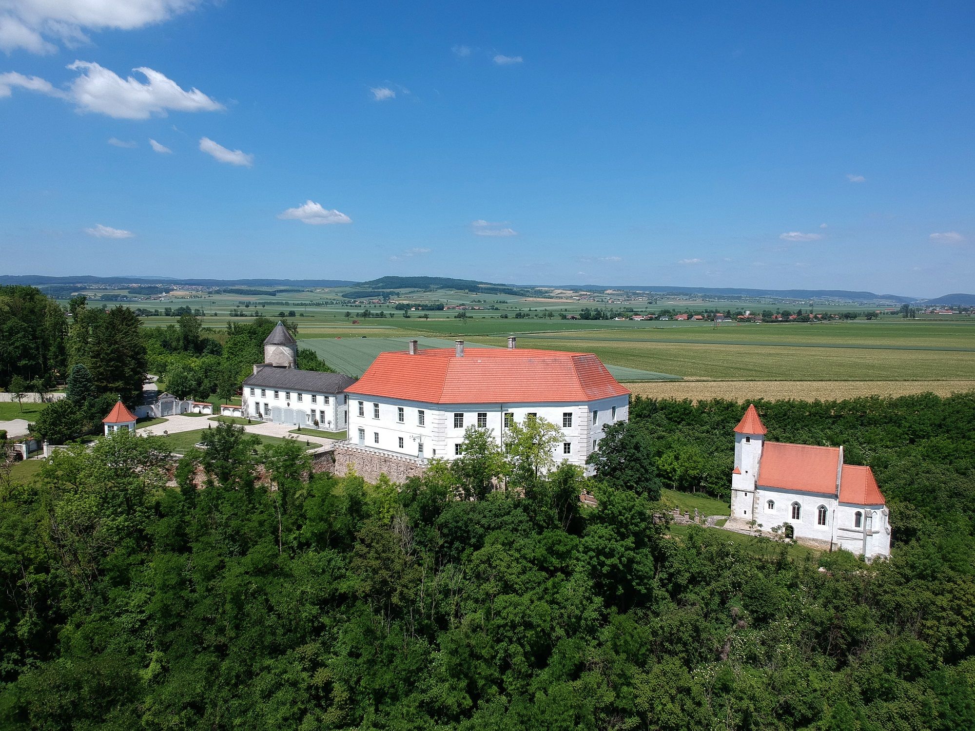 Luftaufnahme von Schloss Viehofen mit rotem Dach, umgeben von grüner Landschaft und Feldern.