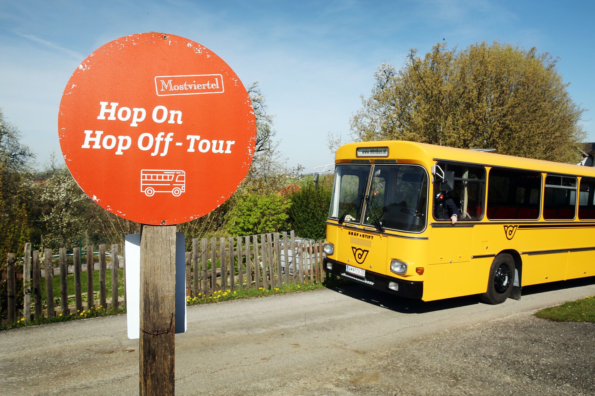 Die Birnbäume blühen in voller Pracht und verleihen der Umgebung einen zauberhaften Duft. Ein nostalgischer Retrobus wartet an der Haltestelle, bereit, die Besucher auf eine unvergessliche Hop On Hop Off Tour durch die malerische Landschaft zu entführen. Genießen Sie die Schönheit der Natur und die frische Luft auf dieser einzigartigen Reise.