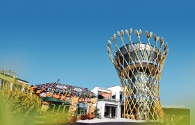 Ein modernes Gebäude mit einem Turm, der von Weizenähren umgeben ist, neben einem dekorativen Knusperhäuschen.