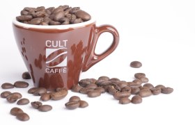 Braune Tasse mit Aufschrift 'Cult Caffè', gefüllt mit Kaffeebohnen, auf weißem Hintergrund.