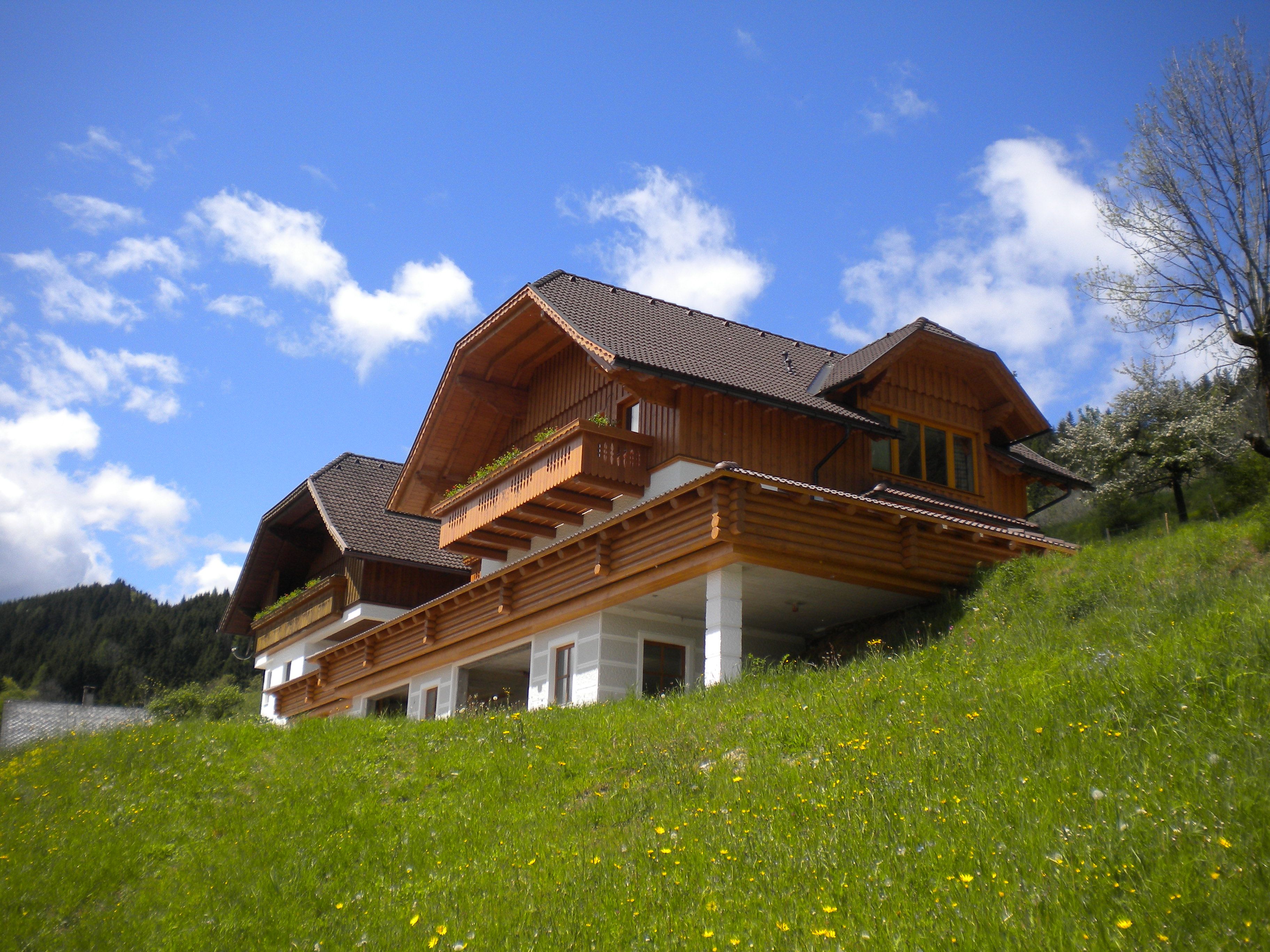 Ein traditionelles Holzhaus auf einem grünen Hügel unter blauem Himmel.