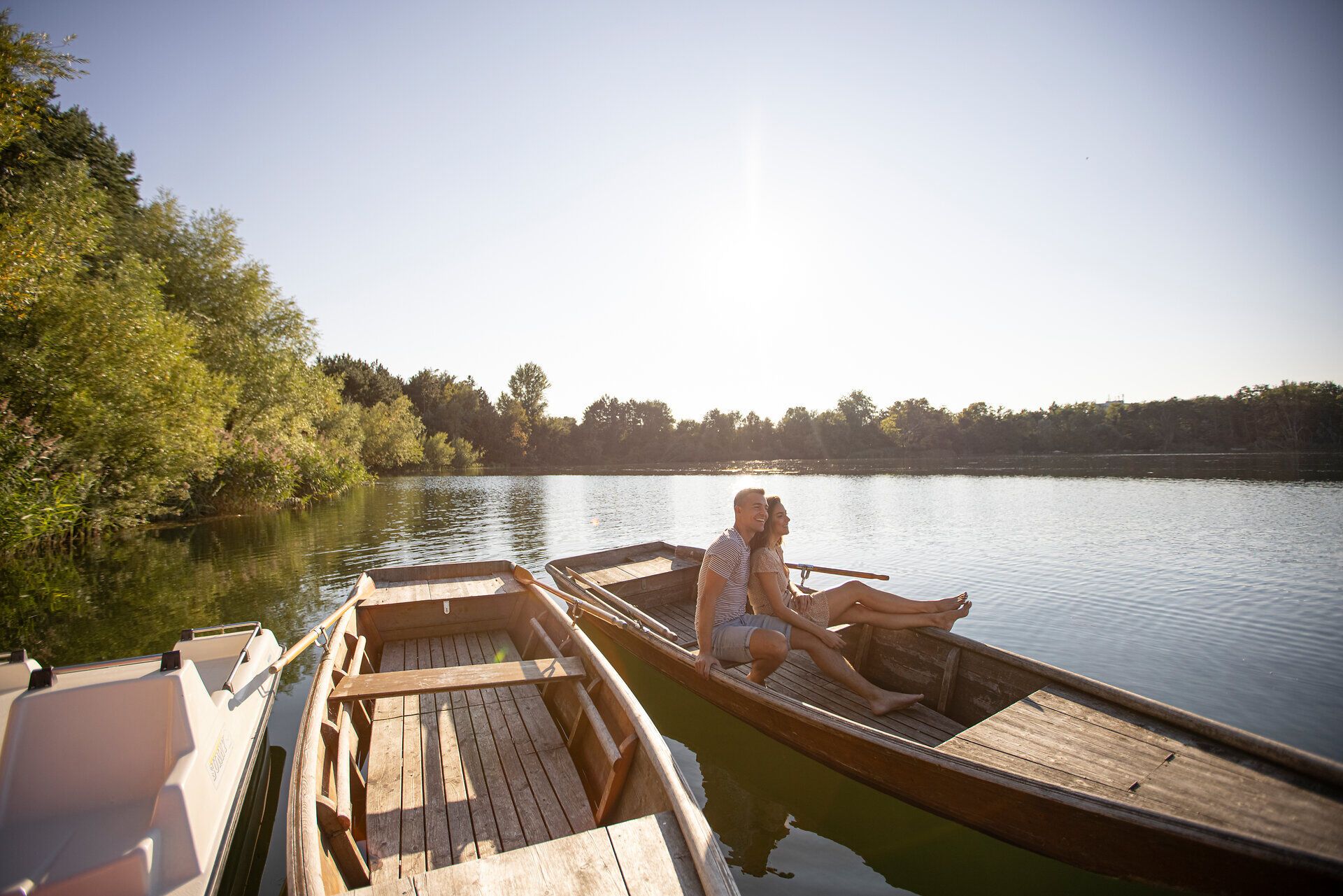 Ein Paar genießt einen romantischen Moment auf einem Boot, umgeben von der ruhigen Schönheit des Wassers und der üppigen Natur. Die sanften Wellen spiegeln die warmen Sonnenstrahlen wider und schaffen eine friedliche Atmosphäre, die zum Entspannen einlädt.