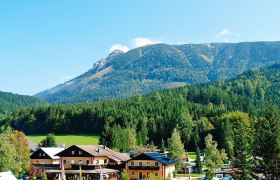 Blick auf ein Campinggel&auml;nde mit Geb&auml;uden vor einem bewaldeten Bergmassiv.