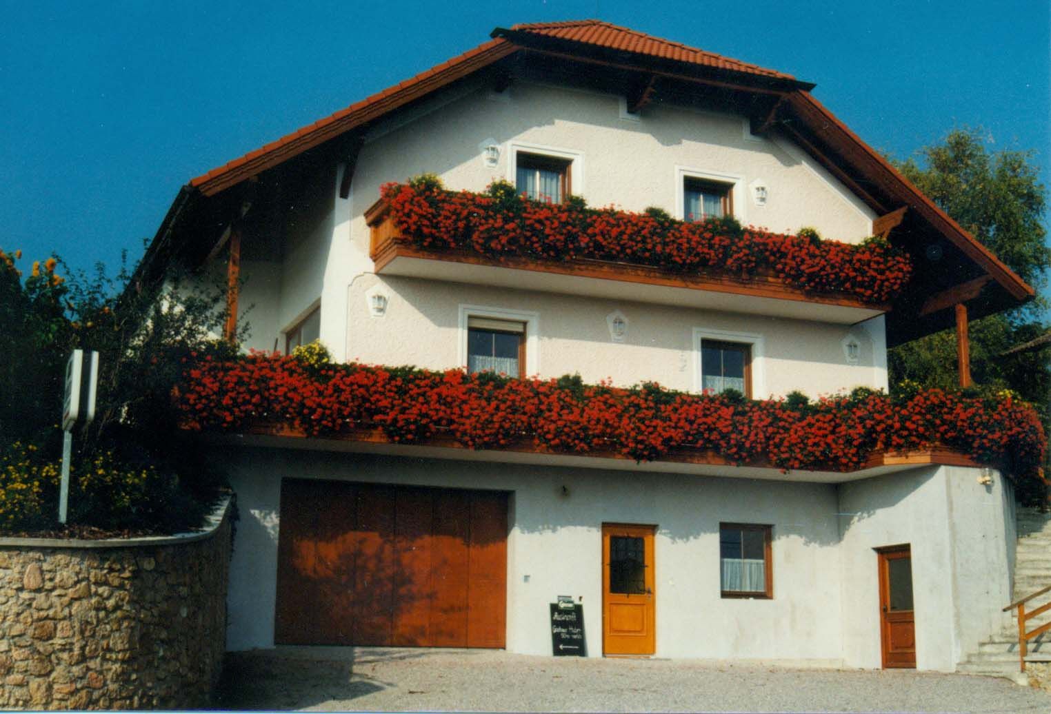 Ein zweistöckiges Gästehaus mit roten Blumen auf den Balkonen.
