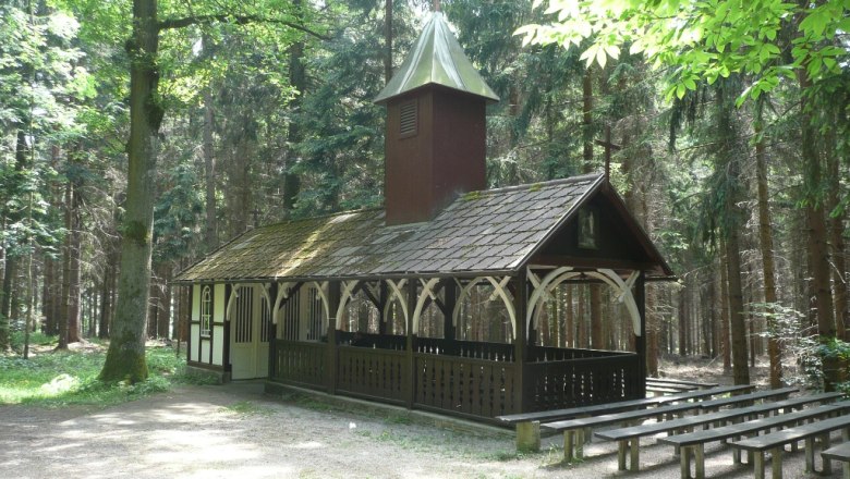 Eine kleine Kapelle im Wald mit Holzbänken im Freien.