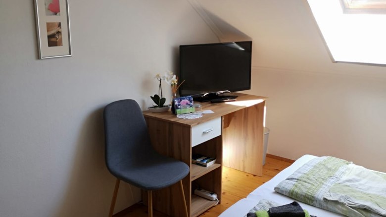 A cozy room with a bed, a small desk with TV, a chair and a skylight.