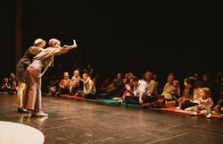 Kinder mit ihren Eltern im Publikum, im Vordergrund zwei Akteurinnen auf einer Bühne