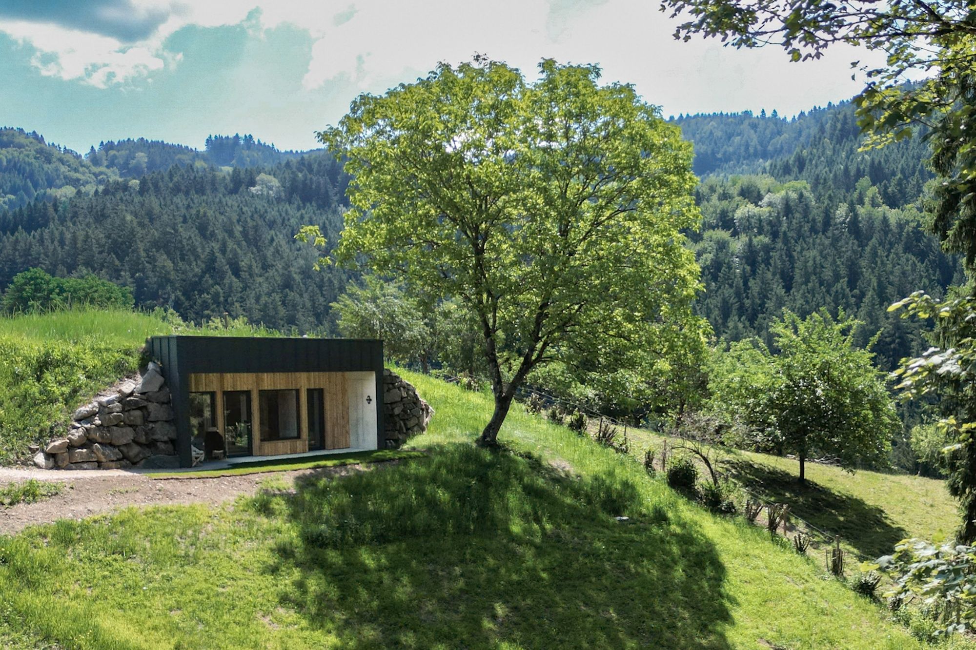 Ein kleines, modernes Haus in einer grünen, hügeligen Landschaft.
