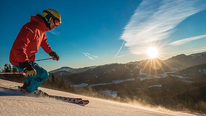 Die frisch präparierten Pisten laden zu einem unvergesslichen Skitag ein, während die Sonne langsam über den Horizont steigt und die schneebedeckten Berge in goldenes Licht taucht. Ein Skifahrer gleitet elegant durch den glitzernden Schnee und genießt die klare, kalte Luft, die den Geist erfrischt und die Sinne belebt.