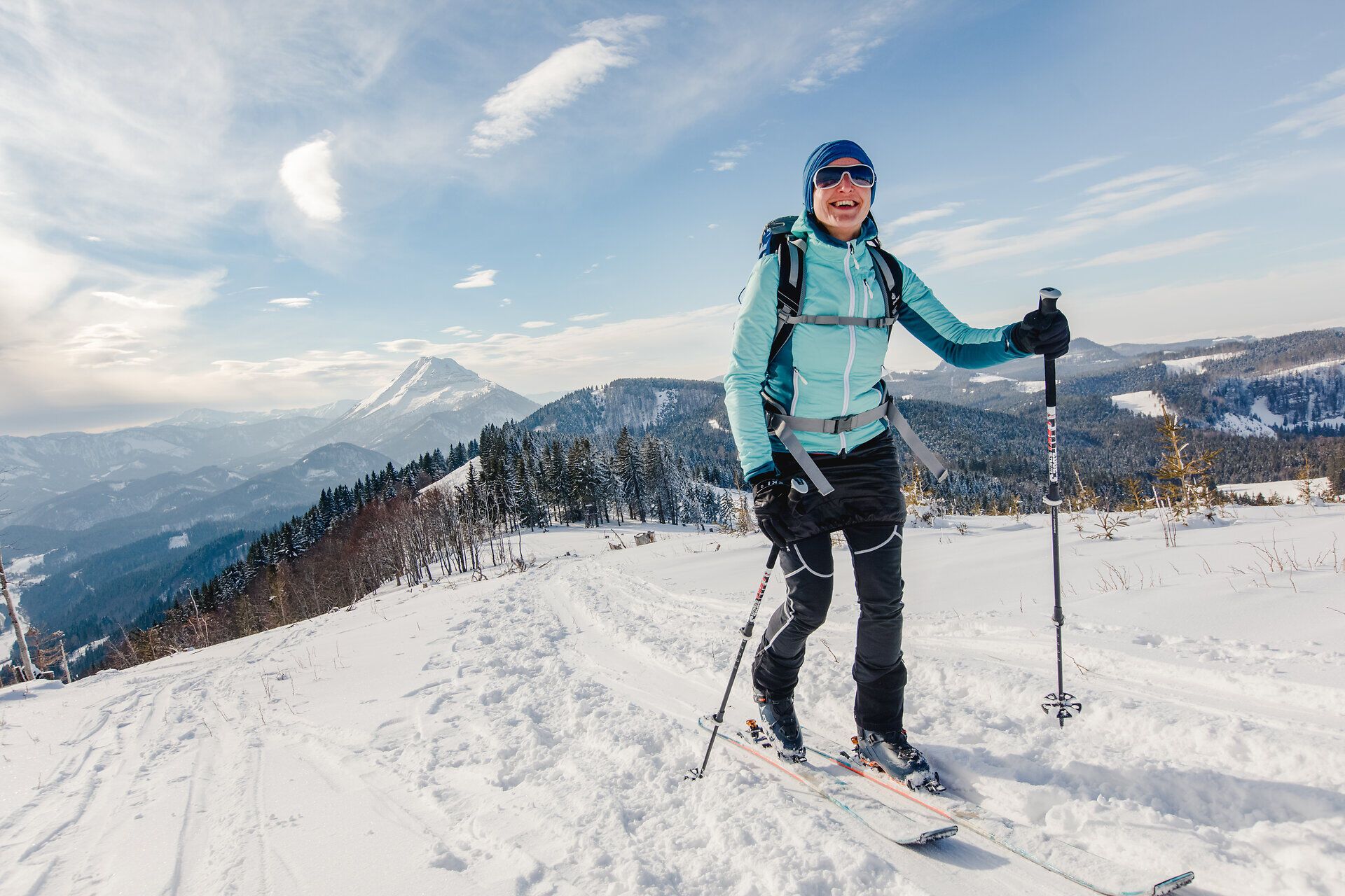 Die strahlende Sonne erhellt die schneebedeckten Hänge, während ein fröhlicher Skitourengeher mit einem breiten Lächeln die unberührte Winterlandschaft genießt. Umgeben von majestätischen Bergen und glitzerndem Schnee, lädt diese idyllische Kulisse zu unvergesslichen Abenteuern in der Natur ein.