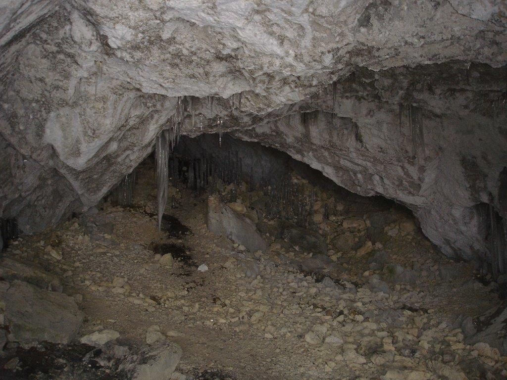 Innenansicht einer trockenen Höhle mit Stalaktiten und steinigem Boden.