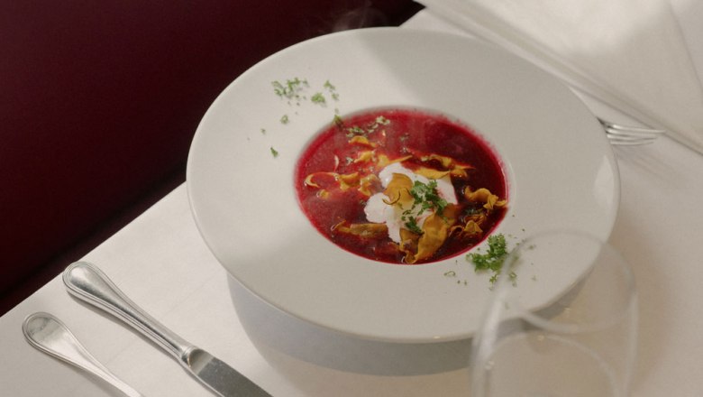 Ein Teller mit roter Rübensuppe, garniert mit Sahne und Kräutern, auf einem gedeckten Tisch.