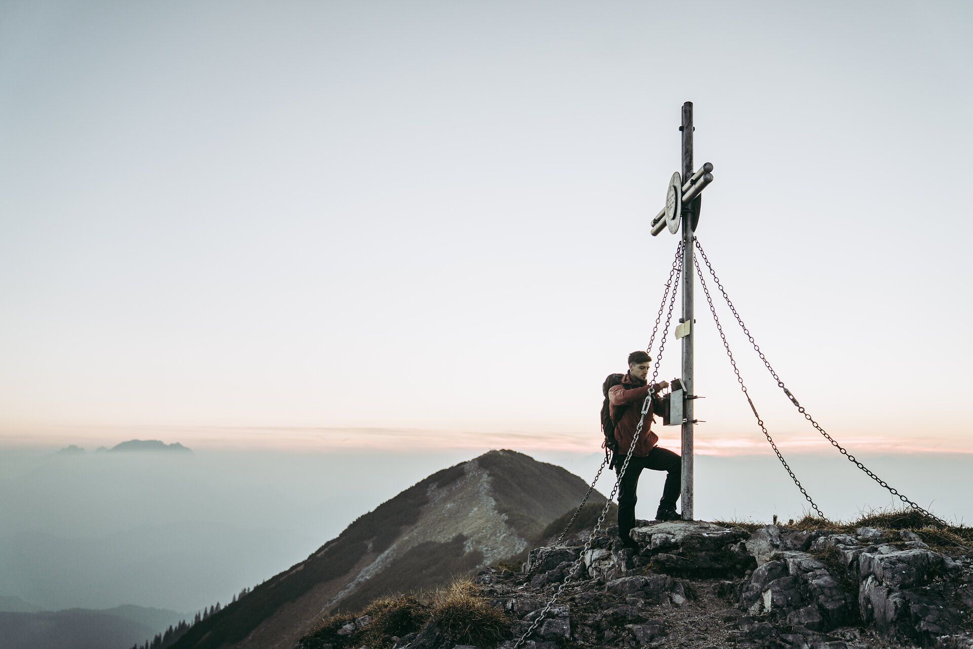 Ein Wanderer erklimmt den Gipfel und genießt den atemberaubenden Ausblick auf die umliegenden Berge. Die frische Bergluft und die ruhige Atmosphäre laden dazu ein, einen Moment innezuhalten und die Schönheit der Natur zu bewundern. Hier, wo Himmel und Erde aufeinandertreffen, wird jeder Schritt zu einem unvergesslichen Erlebnis.