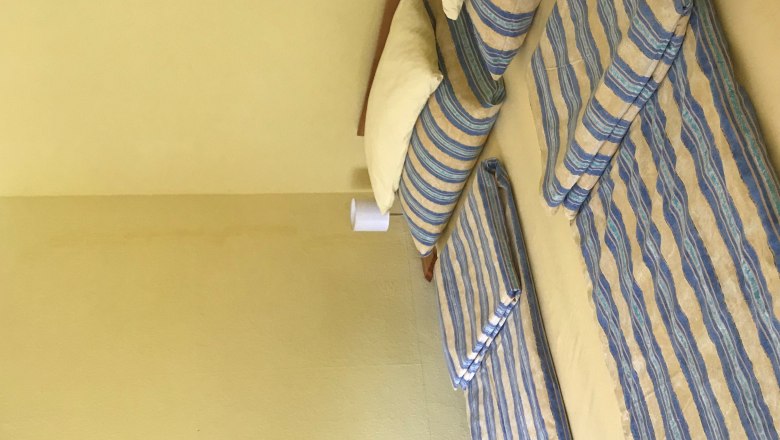 Schlafzimmer mit Doppelbett, gestreifte Bettwäsche, gelbe Wände, kleines Bild an der Wand.