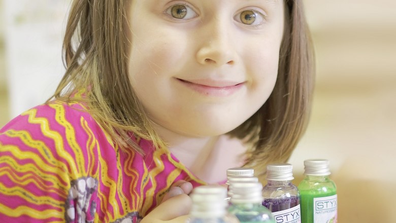 A child in a colorful top smiles next to small bottles of shower gel.