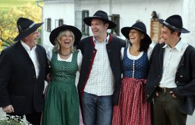 Gruppe von fünf Personen in traditioneller bayerischer Tracht, die fröhlich lachen.
