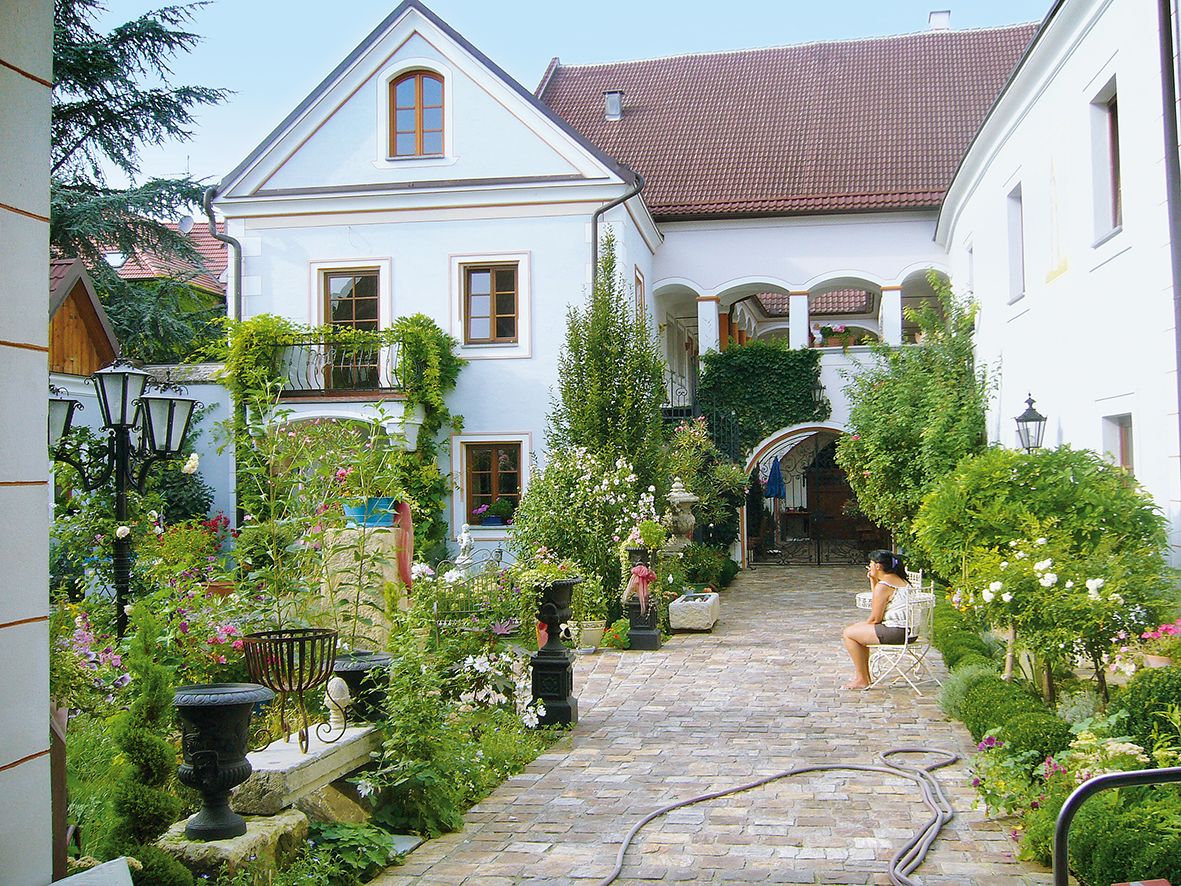 Ein idyllischer Innenhof mit Pflanzen und einer sitzenden Person.