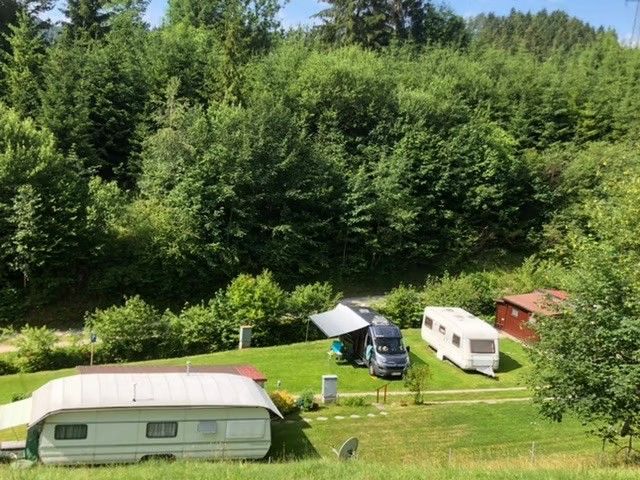 Campingplatz mit Wohnwagen und Wohnmobilen in einer grünen Waldumgebung.