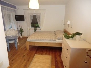 Cozy room with double bed, wooden floor, chest of drawers and small table with chairs.