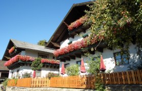 Traditionelles Bauernhaus mit Blumen an den Balkonen und einem Holzzaun im Vordergrund.