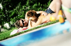 Ein Paar liegt entspannt auf einer Wiese neben einem Pool.