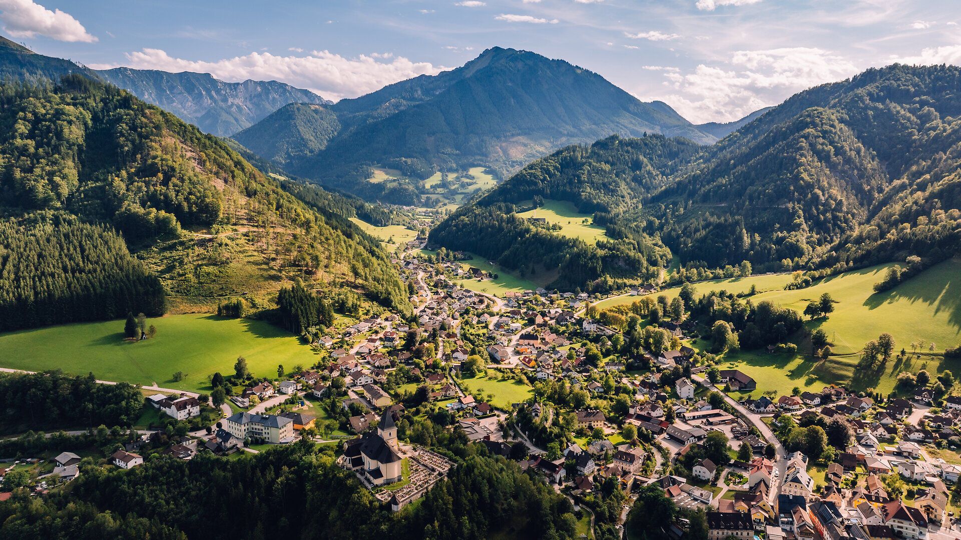 Luftaufnahme von Hollenstein an der Ybbs im Mostviertel mit dem Ortszentrum im grünen Ybbstal, umgeben von bewaldeten Bergen und Wiesen der Ybbstaler Alpen.