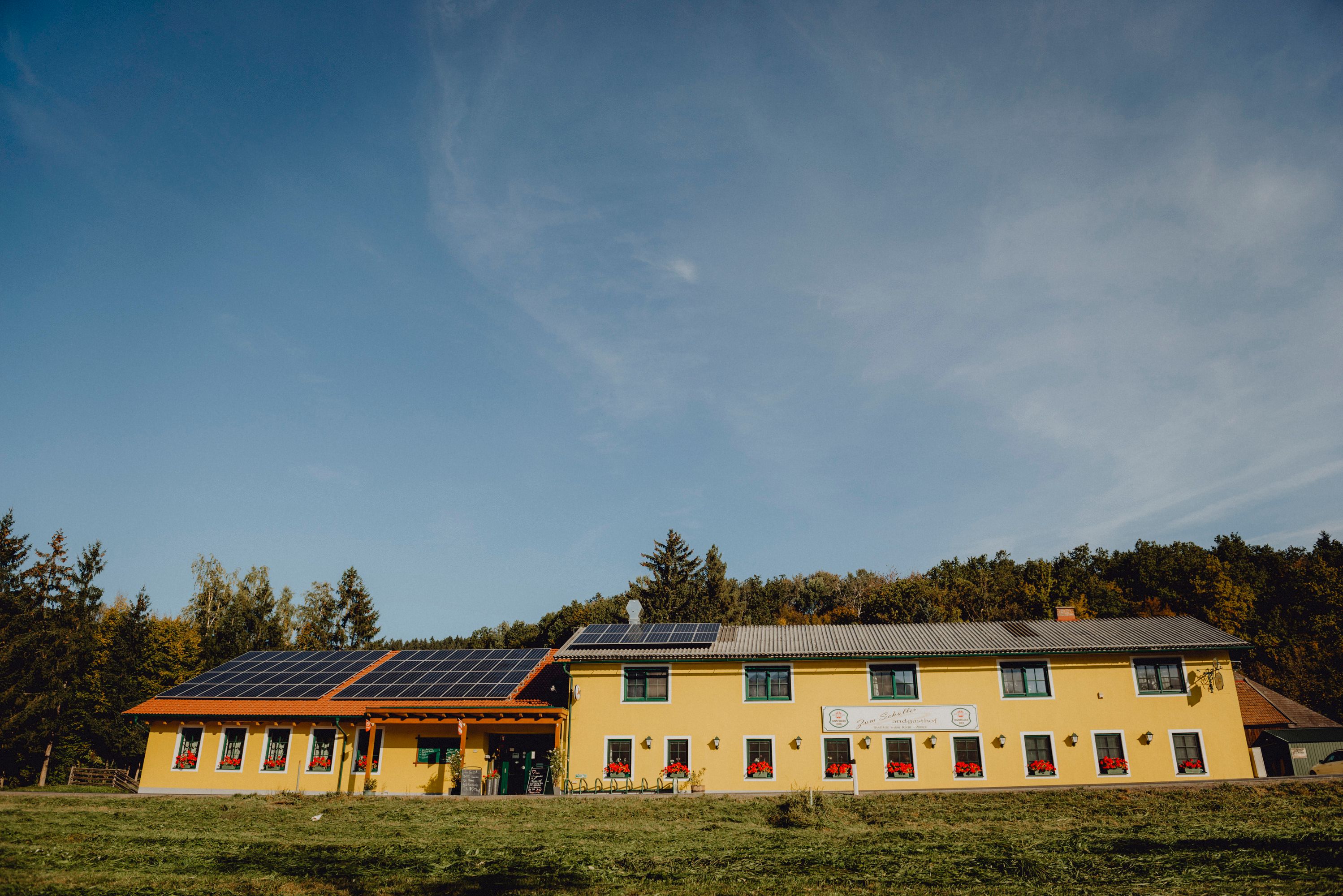 Gelbes Gebäude mit Solarpanelen auf dem Dach, umgeben von Bäumen.