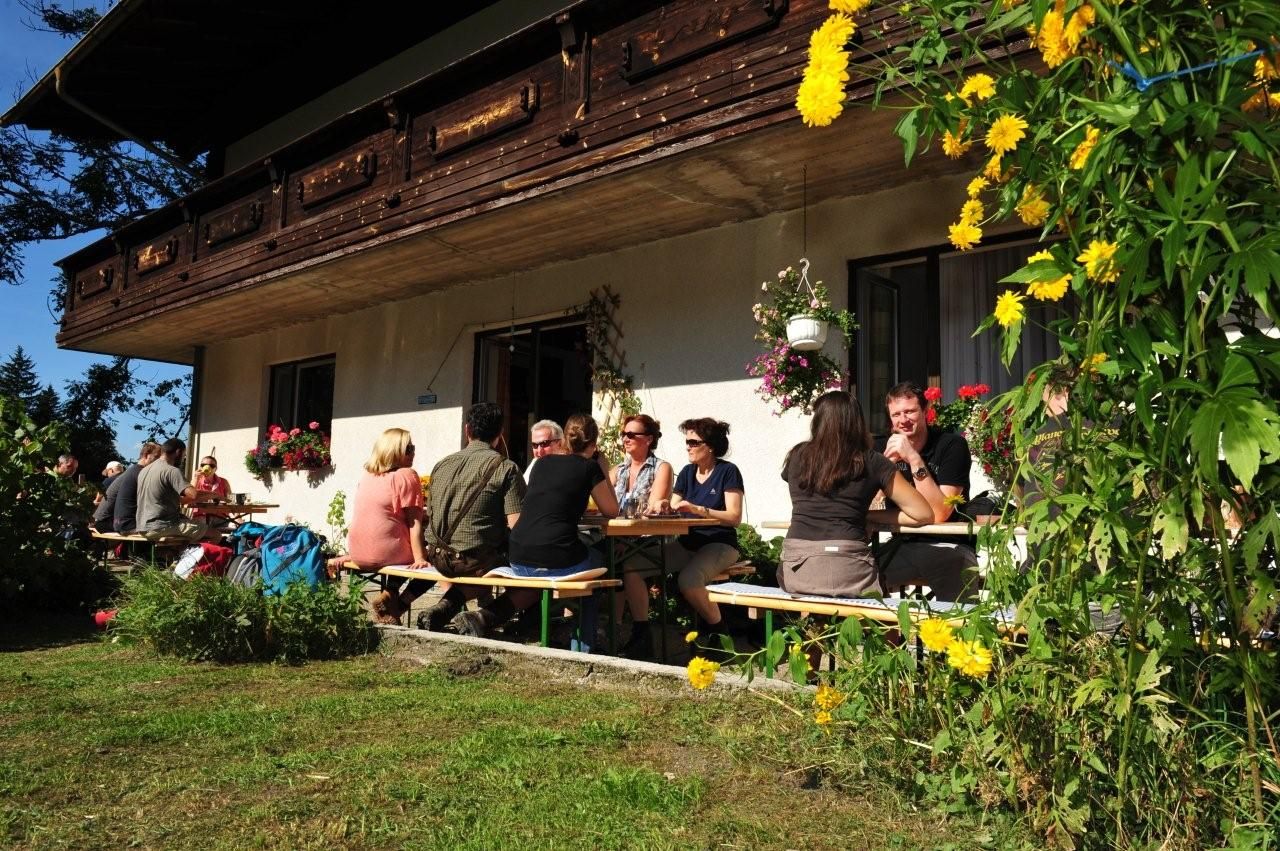 Menschen sitzen an Tischen vor einem Bauernhaus im Freien.