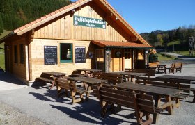 Holzhütte mit Tischen im Freien, sonniger Tag.