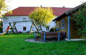 Ein Spielplatz mit Schaukel, Rutsche und Sitzbänken vor einem Haus mit rotem Dach.