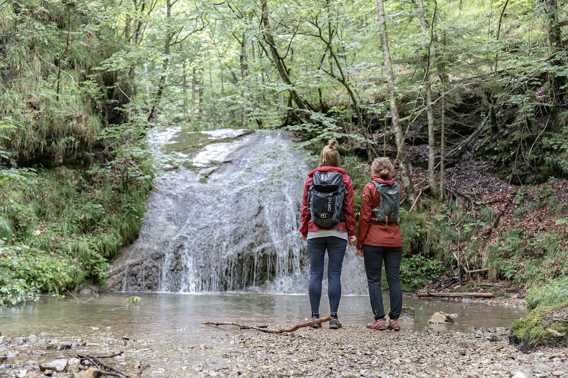 Umgeben von üppigem Grün und dem sanften Plätschern des Wassers, stehen Wanderer am Ufer und genießen die erfrischende Brise. Die Kogler Wasserfälle präsentieren sich in voller Pracht und laden dazu ein, die Schönheit der Ybbstaler Alpen hautnah zu erleben.