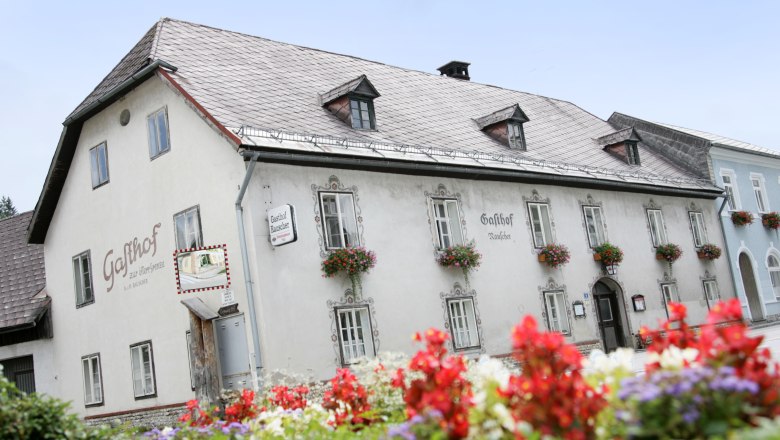 Ein traditionelles Gasthaus mit Blumen an den Fenstern und einem Schild mit der Aufschrift 'Gasthof Rauscher'.
