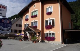 Ein dreistöckiges Gebäude mit orangefarbener Fassade und Blumenkästen vor den Fenstern. Ein Schild mit der Aufschrift 'Puntigamer' ist sichtbar.