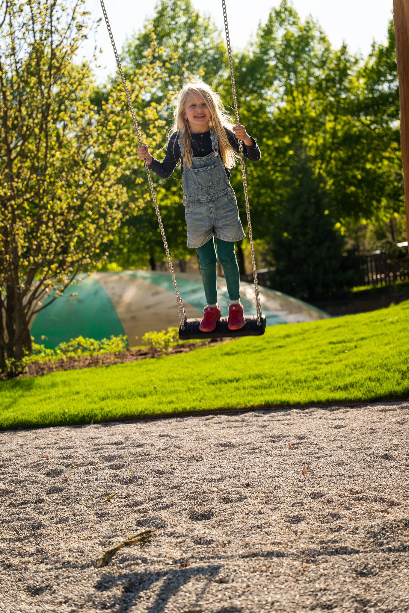 Ein Kind schaukelt fröhlich auf einem Spielplatz im Grünen.
