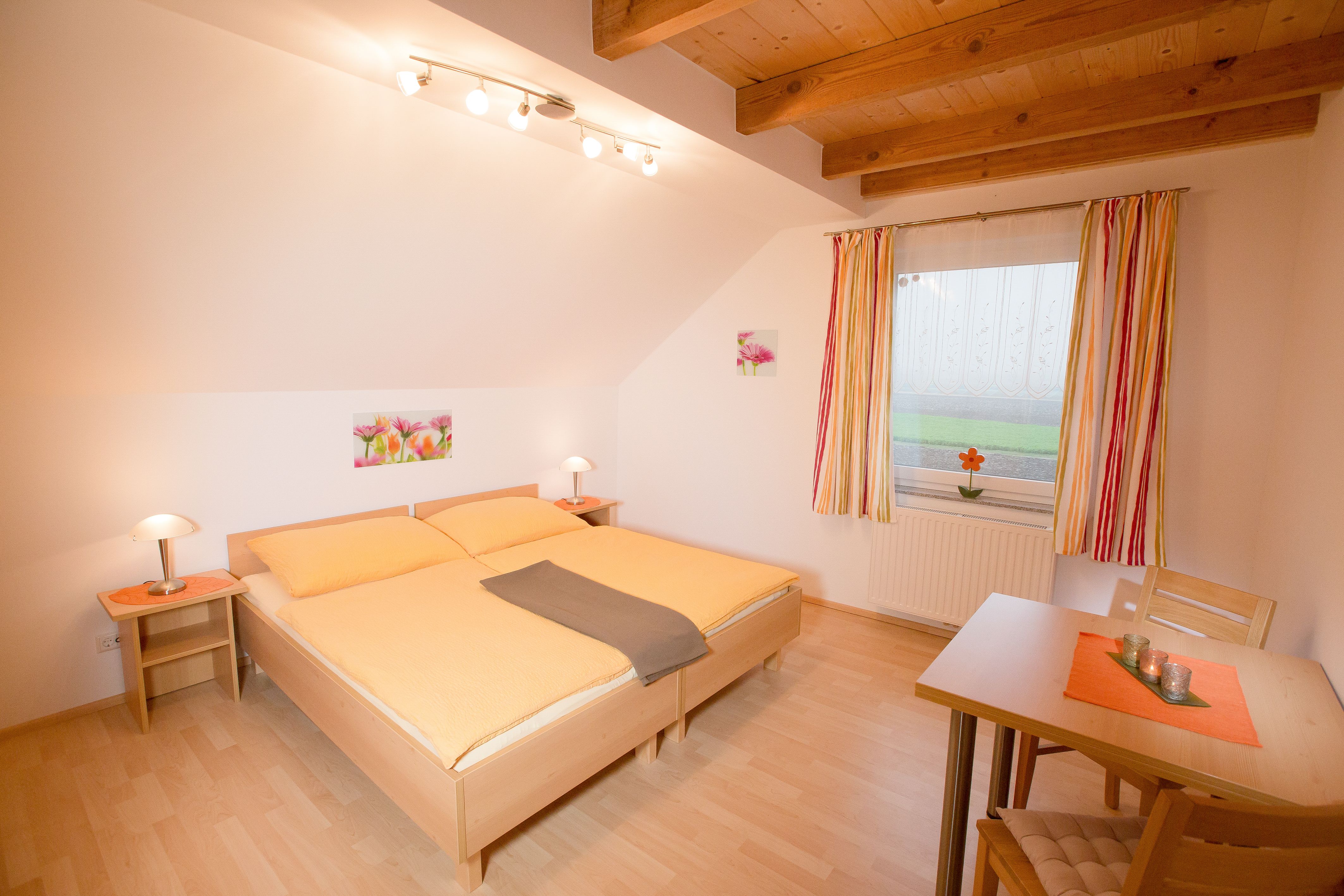 Gemütliches Schlafzimmer mit Doppelbett, Holzbalkendecke und Tisch mit Stühlen.