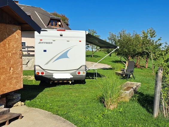 Wohnmobil auf einem grünen Stellplatz beim Camping am Hof Rabenberg mit Markise, Stühlen und Gartenblick.