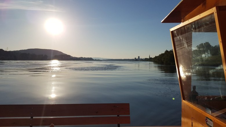 Sonnenuntergang über einem ruhigen Fluss mit einem Holzboot im Vordergrund.
