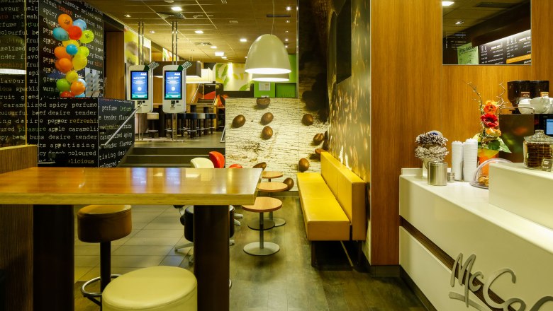 Innenansicht eines McDonald's Restaurants mit McCafé-Bereich, Sitzgelegenheiten und Bestellterminals.