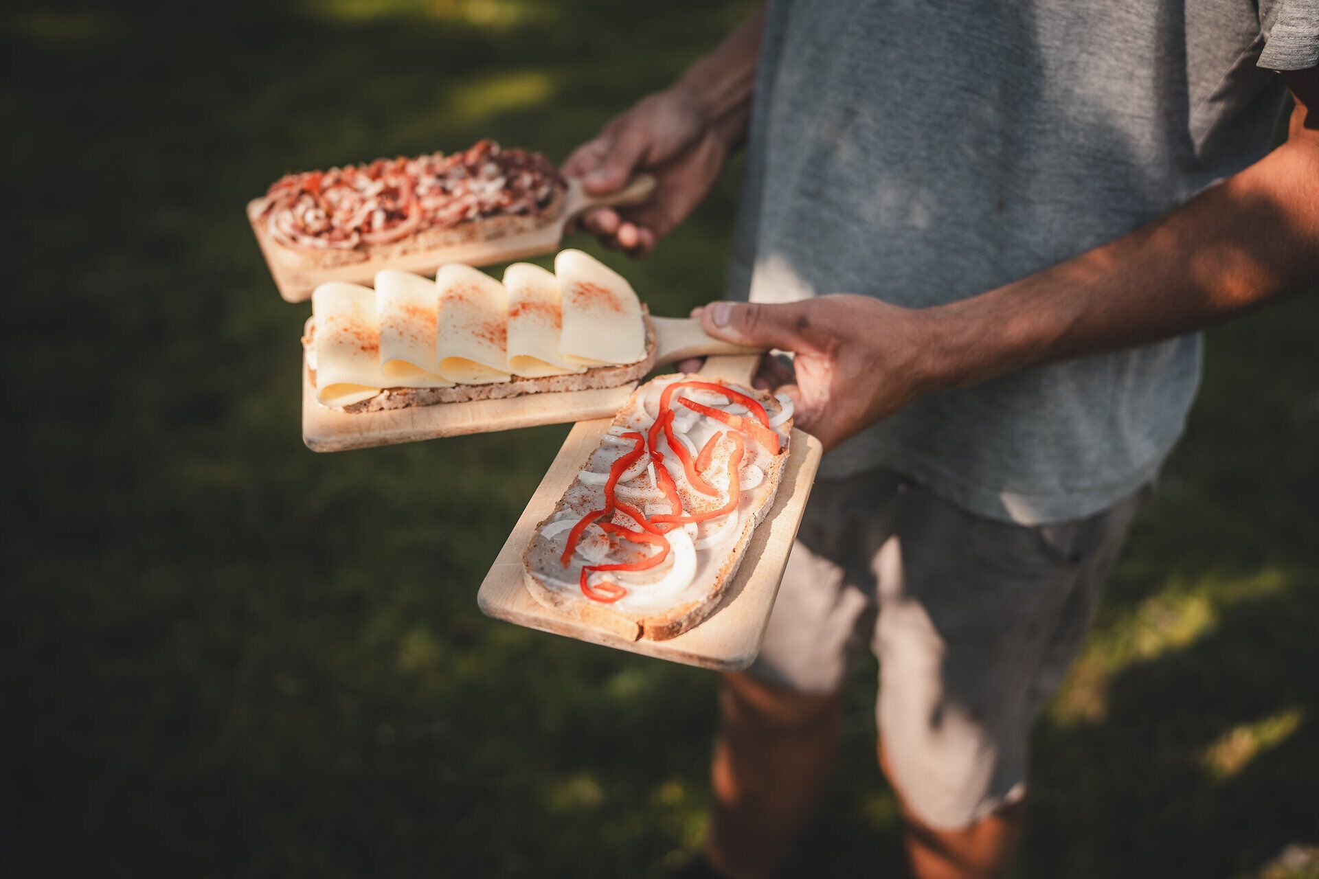 Person trägt ein Holzbrett mit traditioneller Hüttenjause auf der Herrenalm. 