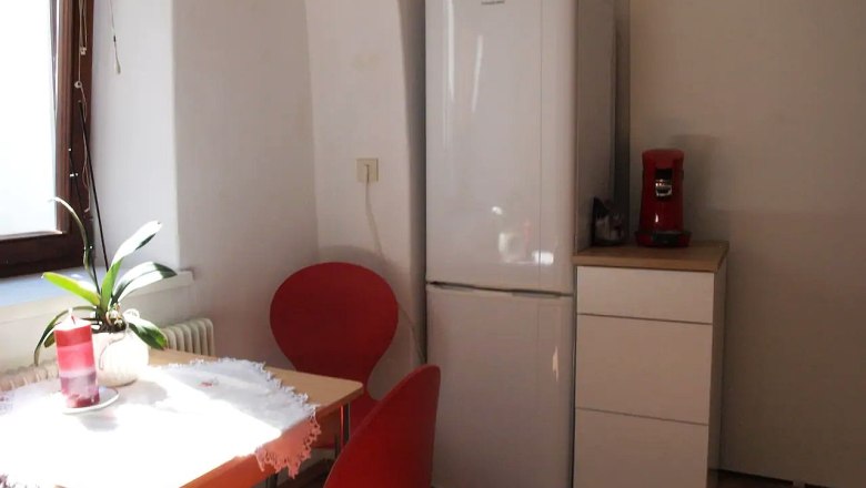 Kleine K&uuml;che mit Tisch, roten St&uuml;hlen, K&uuml;hlschrank und Kaffeemaschine.