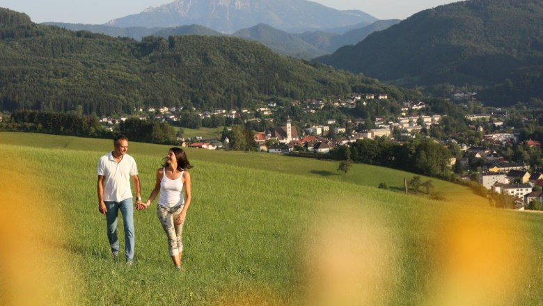Ein Paar spaziert über eine grüne Wiese mit Blick auf die Stadt Scheibbs und umliegende Berge im Hintergrund.