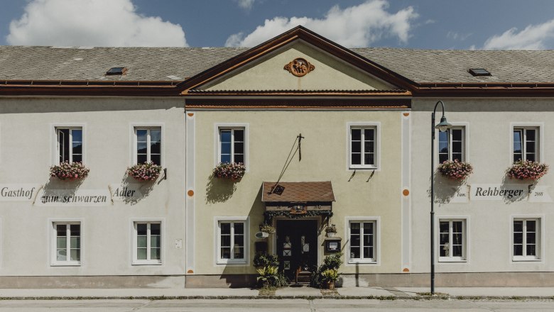 Facade of an inn with flowers on the windows and a sign with the inscription 'Gasthof zum schwarzen Adler'.