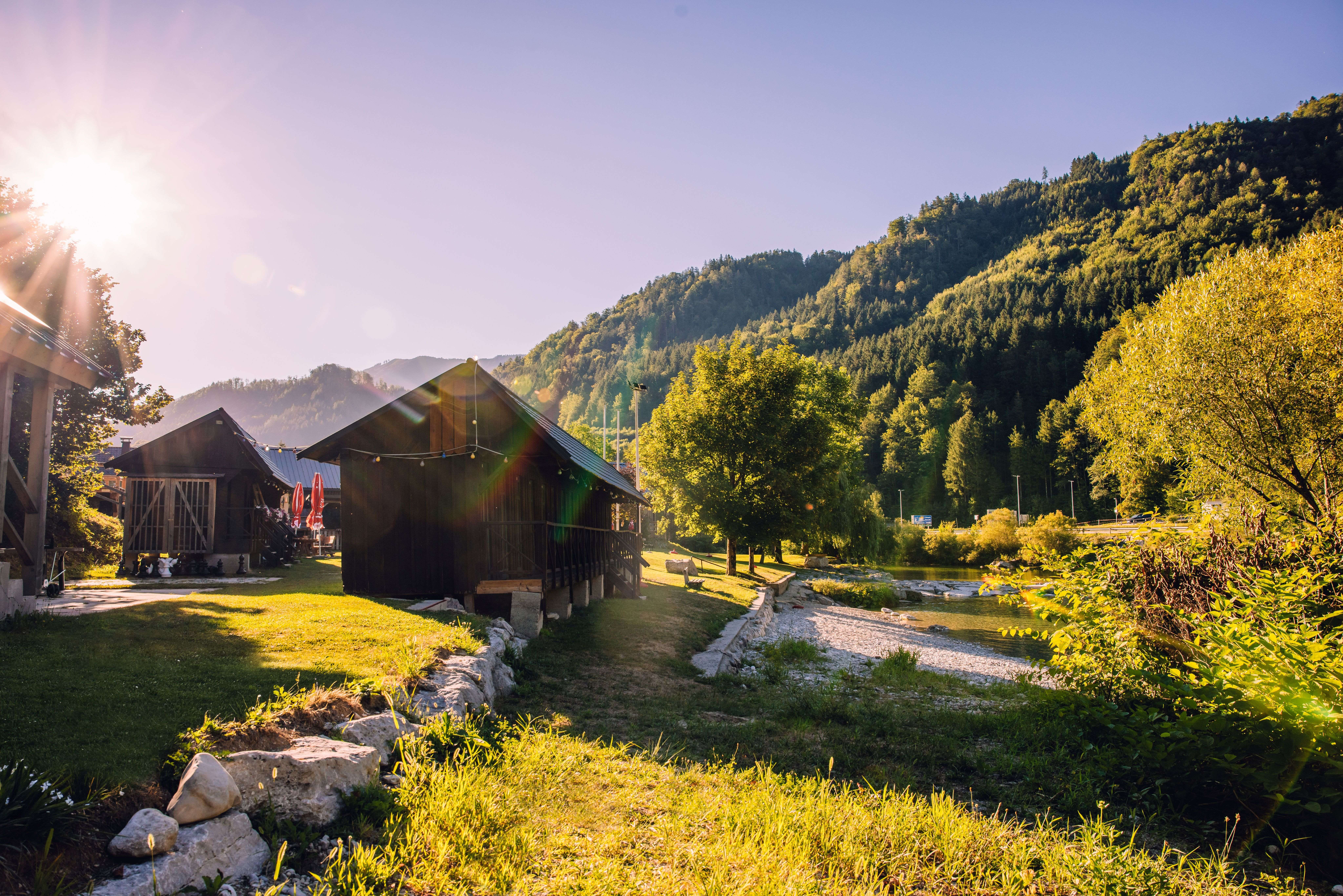 Sonnige Flusslandschaft an der Ybbs in Hollenstein mit Holzhütten, grünen Wiesen und bewaldeten Bergen.